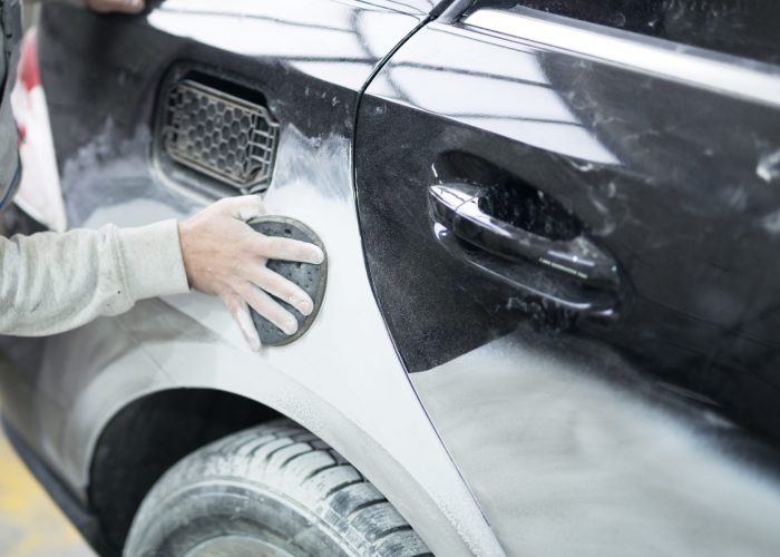 Car painter preparing car for painting in workshop.